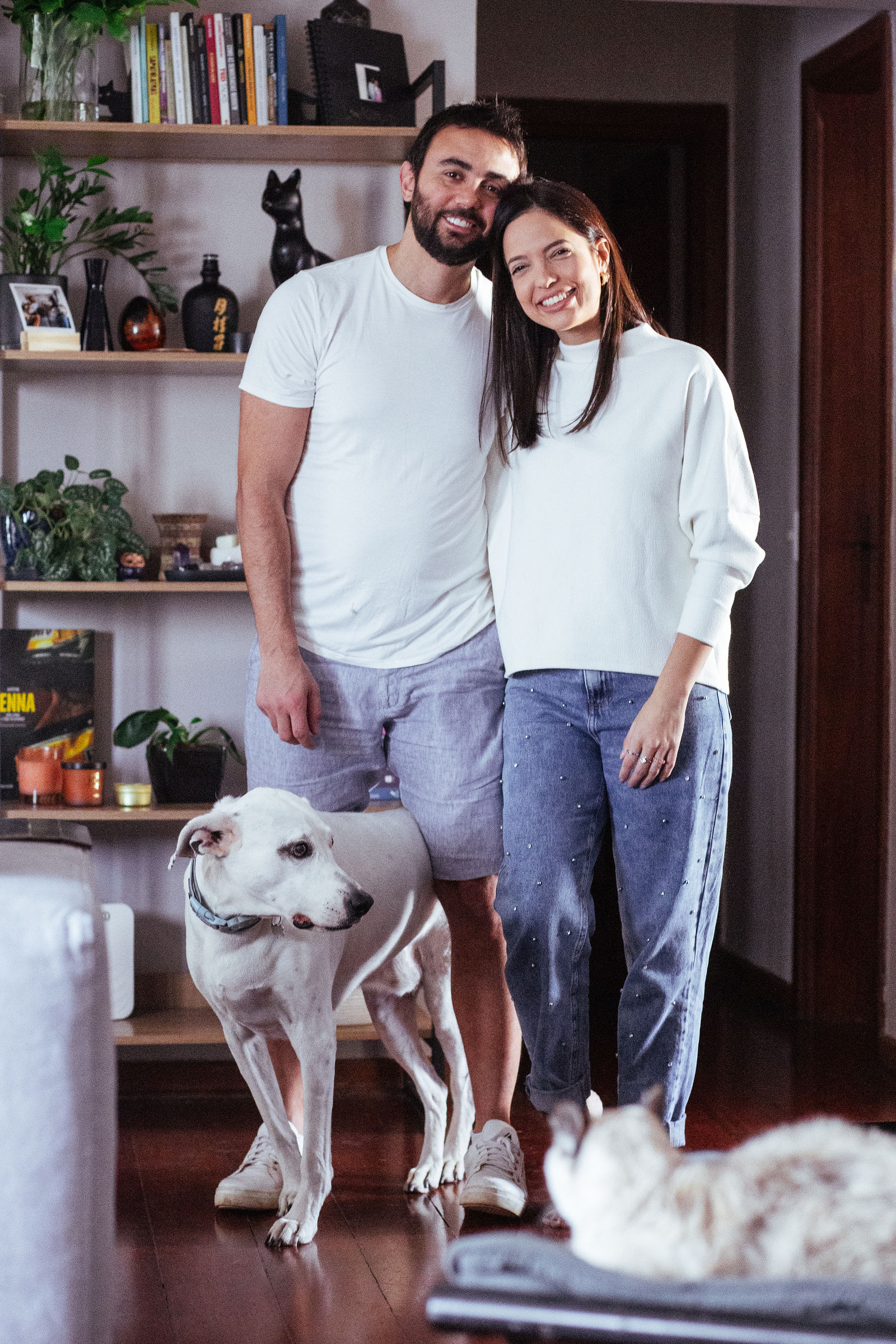 Thais e Leo em pé na sala ao lado do cão branco e da gata deitada